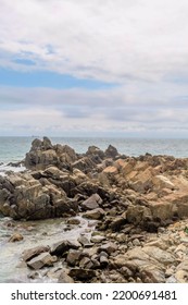 Rock Formations In Ocean Cove Near Craggy Coastline With Ships On Horizon.