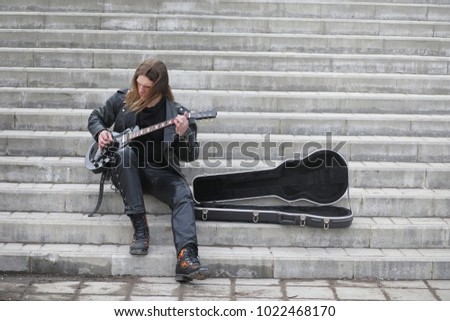 Rock guitarist on the steps. A musician with a bass guitar in a leather suit. Metalist with a guitar on the background of industrial step.
