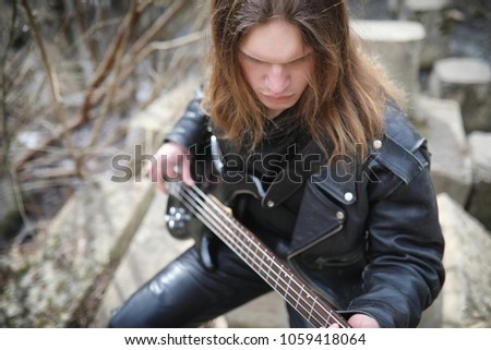 Rock guitarist on the steps. A musician with a bass guitar in a leather suit. Metalist with a guitar on the background of industrial step.