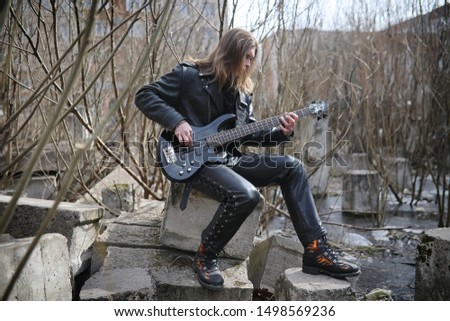 Rock guitarist on the steps. A musician with a bass guitar in a leather suit. Metalist with a guitar on the background of industrial step.
