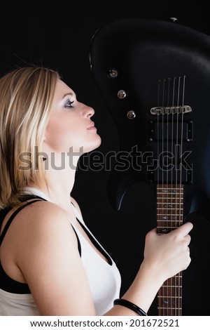 Rock music. Blonde girl guitarist musician performer with electric guitar musical string instrument on black. Concert.
