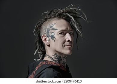 Rock musician. Portrait of a brutal mature man with ethnic tattoos on his head and neck, with mohawk dreadlocks on his head posing on a black studio background. Ethnic rock and punk culture. 