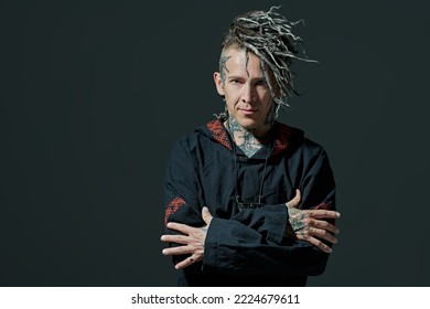 Rock musician. Portrait of a brutal mature man with ethnic tattoos and mohawk dreadlocks on his head posing expressively on a dark studio background. Ethnic rock and punk culture. Copy space.