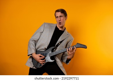 Rock ' N ' Roll Guy, A Cool Guy With A Fake Guitar, Pretends To Play Music. Fun And Emotion. A Guy In A Jacket With A Gaming Guitar, Playing Guitar In A Simulator