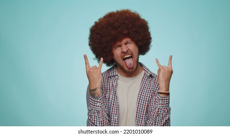 Rock N Roll. Overjoyed Delighted Man 30 Years Old In Shirt Showing Gesture By Hands, Cool Sign, Shouting Yeah With Crazy Expression, Dancing, Emotionally Rejoicing In Success Win Alone On Blue Wall