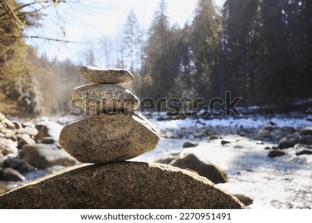 Rock pile or stack in front of defocused river and forest on a sunny day. Pebble tower or rock pyramid. Concept for relaxing, zen, spiritual or yoga. Nature background. Selective focus on rocks.