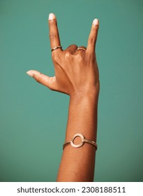 Rock and roll hand sign by a studio for party, cool or wild greeting with rings and bracelet jewelry. Emoji, punk and woman rebel or rocker gesture with fingers isolated by a dark green background. - Shutterstock ID 2308188511
