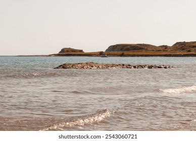 Rock in the sea against rocky hills on a Mediterranean island - Powered by Shutterstock