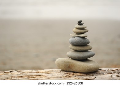 Rock Stacking On A Large Piece Of Driftwood Along The Washington Coast.