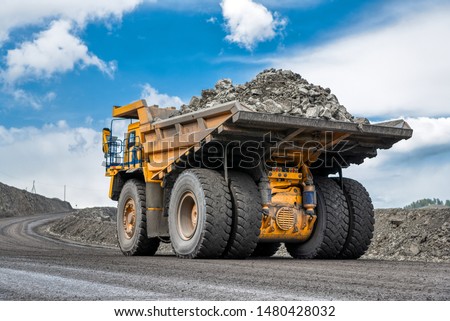 Rock transportation by dump trucks. Large quarry yellow truck. Transport industry. Mining truck is driving along a mountain road.