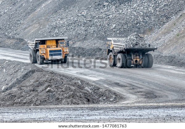 Rock transportation by dump trucks. Large quarry\
yellow truck. Transport industry. Mining truck is driving along a\
mountain road.