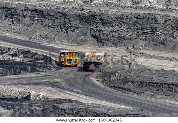 Rock transportation by dump trucks. Large quarry\
yellow truck. Transport industry. Mining truck is driving along a\
mountain road.