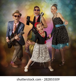 Rockabilly Family Band Playing Music And Singing On A Black Background With Glowing Lights
