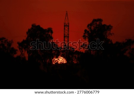 Rocket launch at sunset with trees silhouetted against vibrant red sky and fiery glow