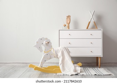 Rocking horse with plaid and chest of drawers near light wall