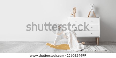 Rocking horse with plaid and chest of drawers near white wall in room