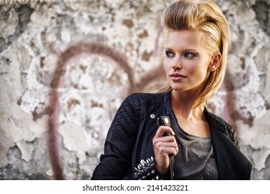 Rocknroll fashion. An edgy young woman holding the collar of her leather jacket.