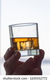 Rocks Glass With Amber Colored Alcohol In Hand With Bright Backlit Background. Vertical Orientation. 