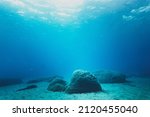 Rocks on sand at bottom of ocean floor in blue clear sea