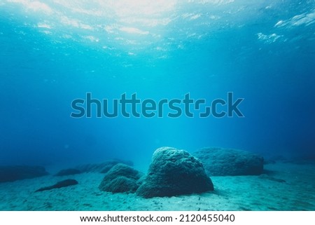 Rocks on sand at bottom of ocean floor in blue clear sea