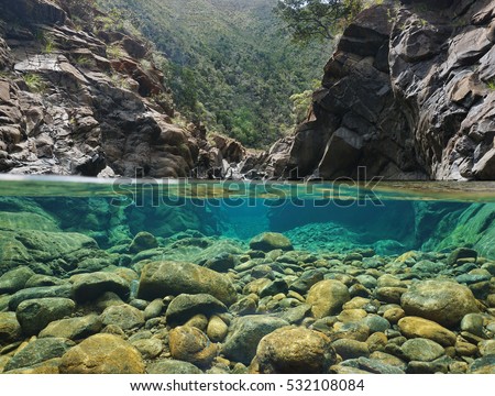 Rocks over and under the water split by waterline in a river with clear water, Dumbea river, New Caledonia
