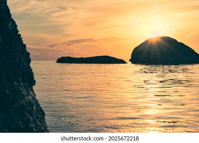 Rocks in the sea at colorful sunrise. The sunbeams of the rising sun sparkle from behind the rock