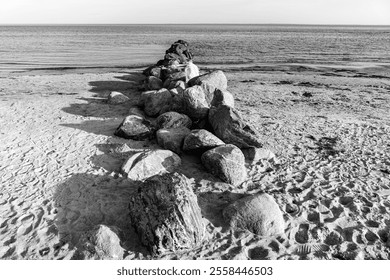 A rocky beach with a large rock formation in the middle. The rocks are scattered across the beach, and the water is calm. The image has a serene and peaceful mood, with the rocks - Powered by Shutterstock