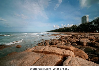 A rocky beach in the morning with calm waves. Behind is a tall white building. - Powered by Shutterstock