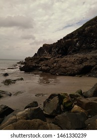Rocky beach scene with the sea to the left of the shot and cliffs the the right.  Dark and and rocks in the for ground. 
