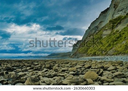 Rocky beach, steep limestone cliffs and a dark, threatening sky at  Whitecliffs, Taranaki region, North Island, New Zealand. Low camera standpoint
