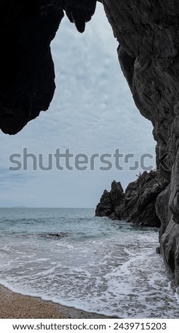 Rocky beach view framed by cave entrance with gentle waves, ideal for background with copy space on left side, tranquil nature concept