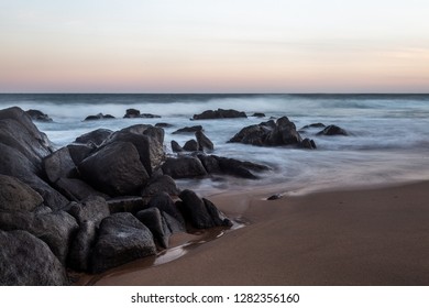 rocky beach with view of rough waves in a blue ocean with a purple, pink, orange blue sky taken from a low angle during sunset in South Africa - Powered by Shutterstock