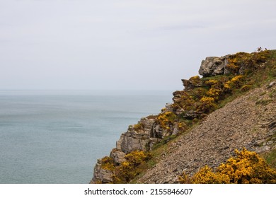 A rocky cliff behind which the ocean can be seen. Cloudy weather.
