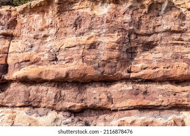 Rocky cliff face showing striations between the different layers of colored rocks, nature backdrop, horizontal aspect