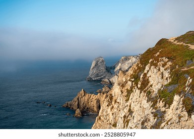 A rocky coastal cliff with mist surrounding the sea stacks in a serene afternoon light - Powered by Shutterstock