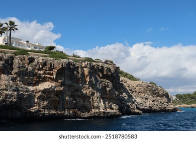 Rocky coastal cliffs of south east Mallorca Majorca, Spain the Mediterranean Sea. Palm trees and plants line the coast and the blue ocean is seen meeting the coastal coves of the Balearic island. - Powered by Shutterstock