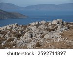A rocky coastal landscape with a view of the sea and distant mountains. Symi island, Greece