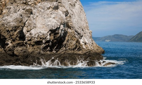 A Rocky coastal landscape with waves crashing against the rocks on a sunny day with distant mountains in the background - Powered by Shutterstock