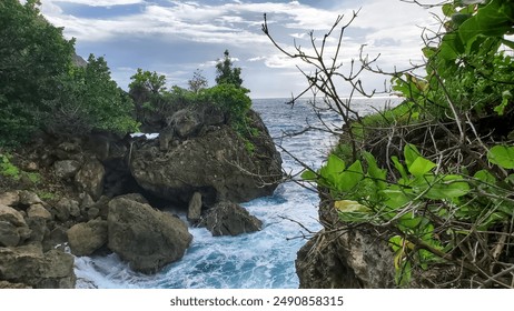 Rocky coastal scene with lush vegetation and waves crashing against the rocks. - Powered by Shutterstock