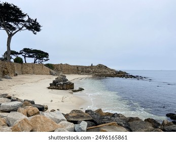 Rocky coastline along Lovers Point Beach near Monterey, California. Water is turquoise blue; rocks are shades of beige and brown. Coast is lined by Monterey Cypress trees. - Powered by Shutterstock