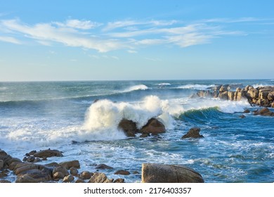 A rocky coastline in the Cape Province, South Africa. Ocean waves crashing on coastal rocks on a sunny summer day with blue clear skies and a scenic tropical landscape beachfront in the Western Cape - Powered by Shutterstock