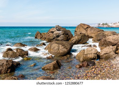 A Rocky Coastline With The City Of Ensenada, Baja California, Mexico In The Background.