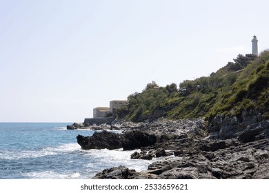 A Rocky coastline with a lighthouse and buildings overlooking the sea under a clear sky - Powered by Shutterstock