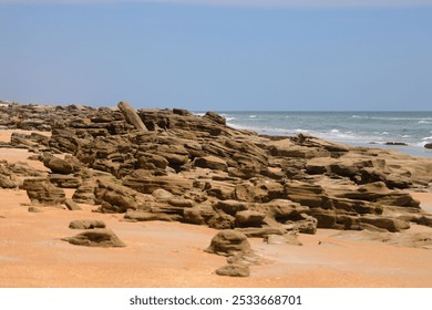 Rocky coastline with sandy beach and ocean waves under a clear blue sky - Powered by Shutterstock