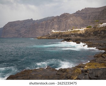 Costa rocosa del sur de Tenerife: acantilados oscuros Los Gigantes y olas azules del Océano Atlántico. Paisaje volcánico de las Islas Canarias, España.