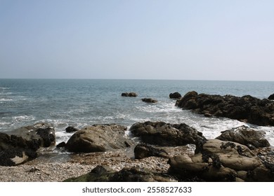 Rocky coastline with waves crashing against the shore, with a clear blue sky - Powered by Shutterstock