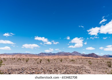 Rocky Desert Valley With Mountains In The Background Under Blue Sky With White Fluffy Clouds.