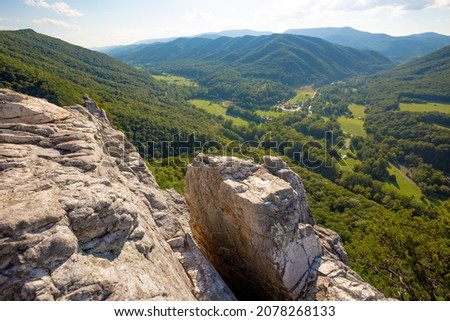 Rocky edge of cliff with outlook view of mountain range and lush green valley with tree in Seneca Rocks