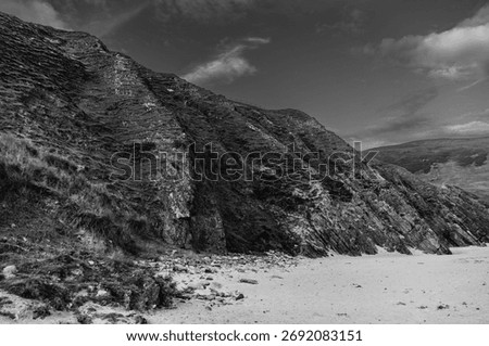 A rocky hillside with a cloudy sky in the background. The hillside is barren and rocky, with no vegetation visible. The sky is overcast, giving the scene a somber and desolate mood