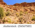 A rocky hillside with sparse vegetation. The sky is clear and blue. Concept of solitude and isolation, as the barren landscape seems to stretch on for miles. The lack of trees